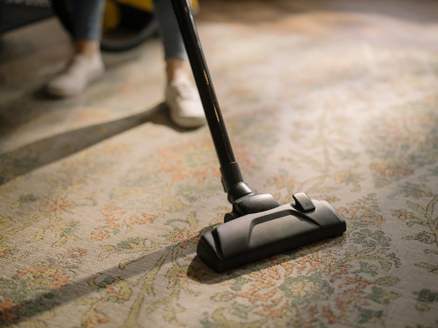 A close-up of a richly patterned, multicolored Oriental rug with intricate floral and geometric designs in shades of red, blue, and beige, laid on a wooden floor. A slightly folded, worn-out hardcover