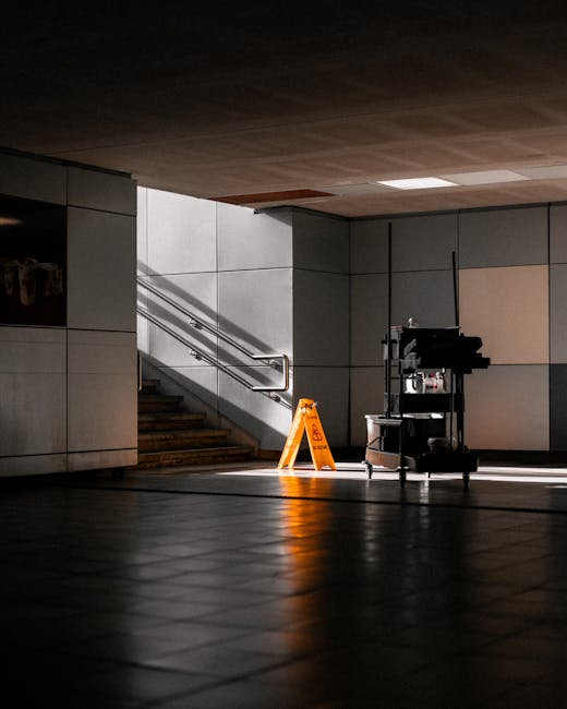 A clean and well-lit underground entrance area featuring smooth, tiled flooring with a polished, reflective surface and a staircase with stainless steel handrails leading upward. The walls are tiled w
